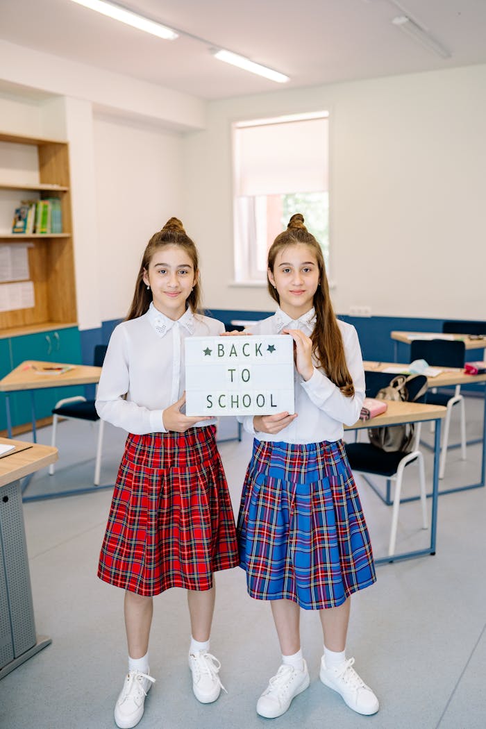 Twin girls in school uniforms holding back to school sign in classroom.
